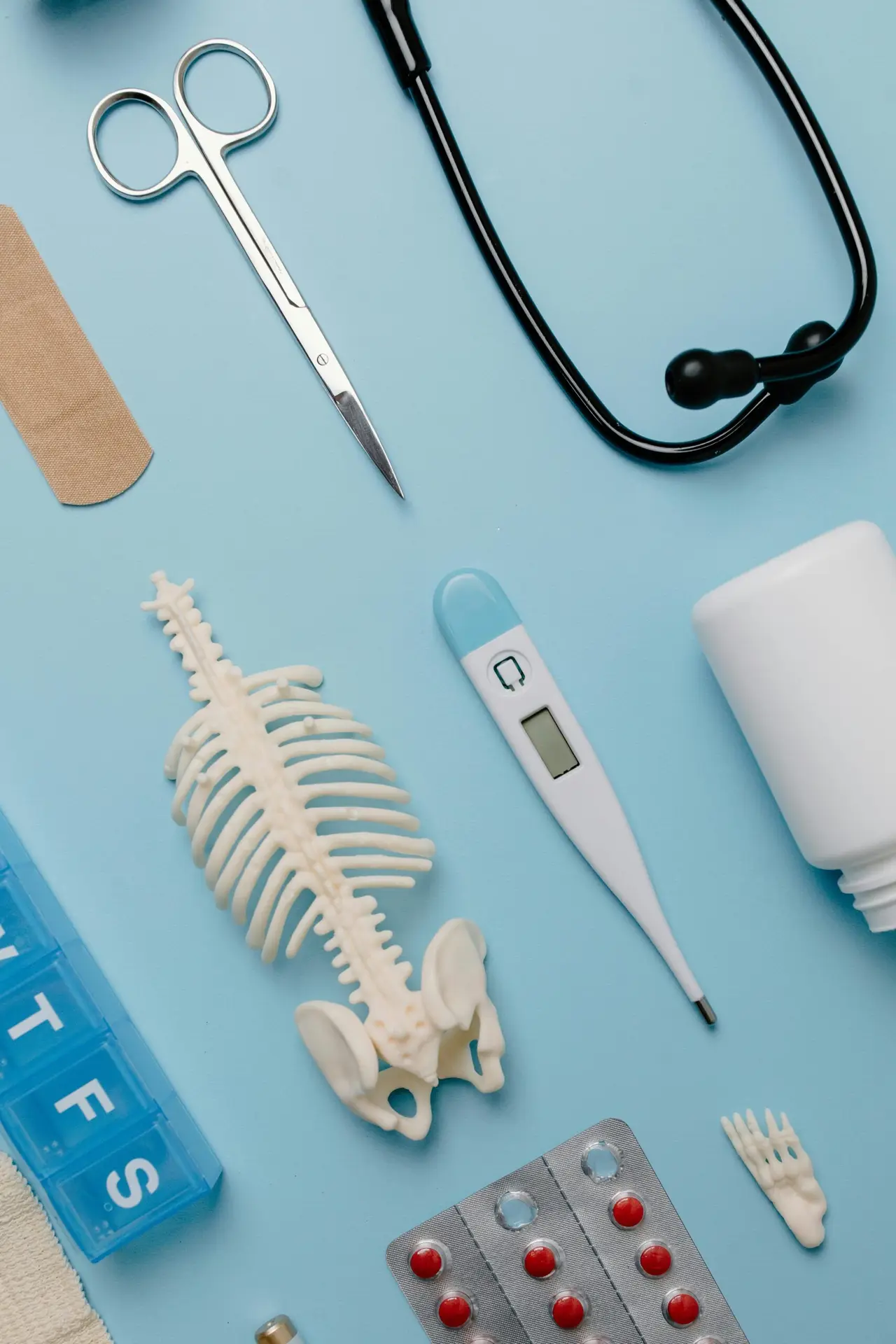 Flat lay of medical tools and skeleton model on a blue background.